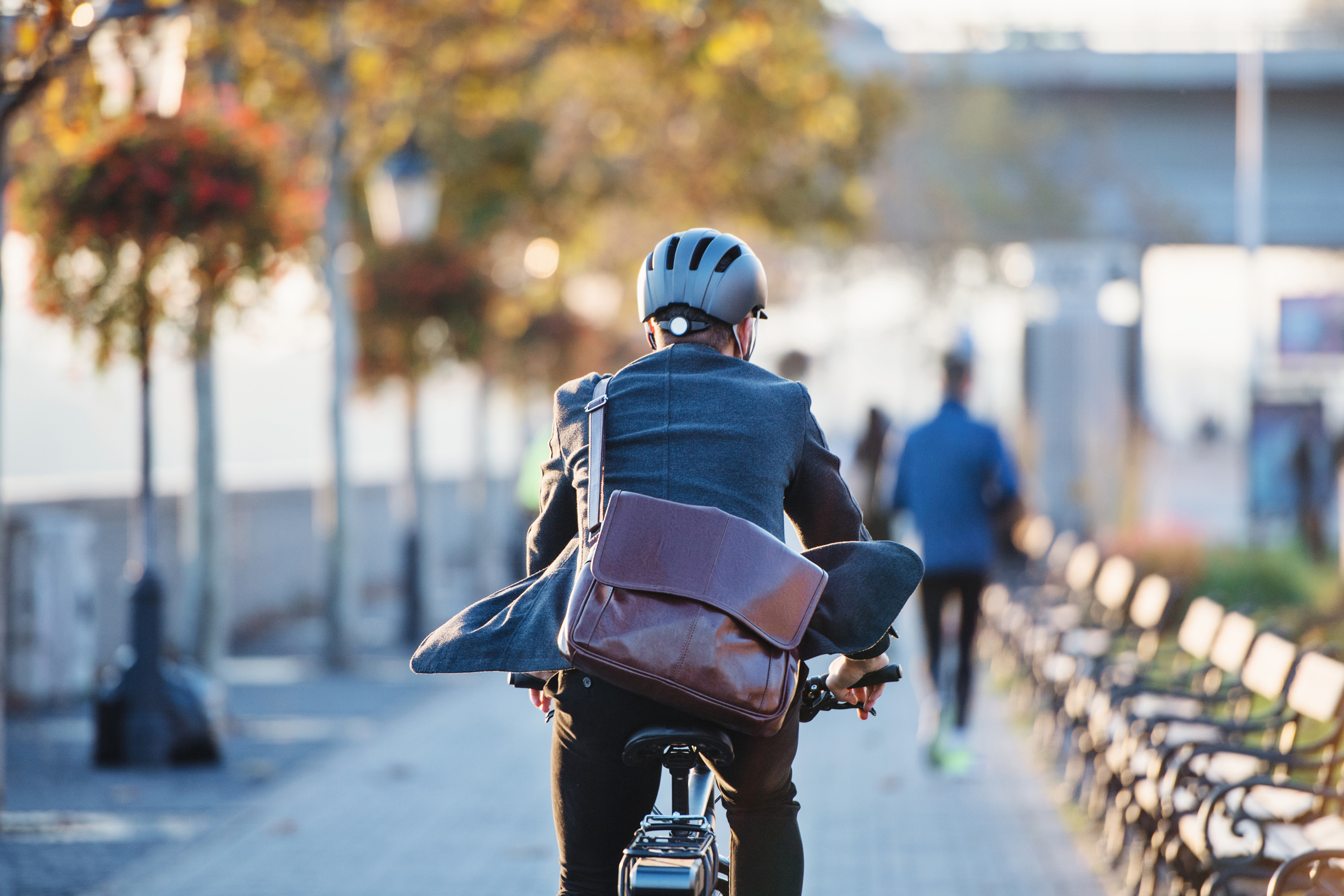 A rear view of a businessman commuter with electric bicycle traveling to work in city. Copy space.