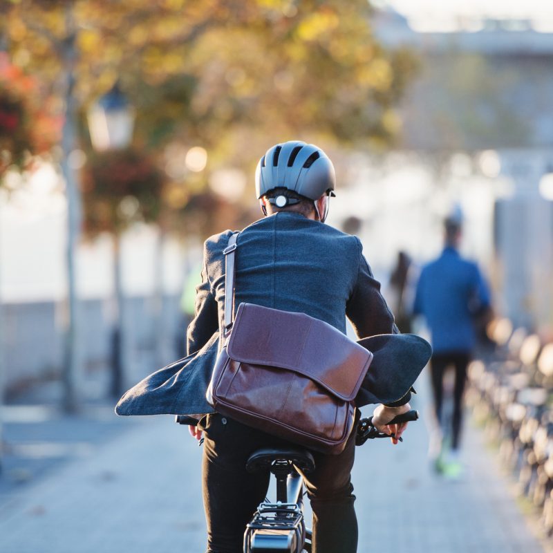 A rear view of a businessman commuter with electric bicycle traveling to work in city. Copy space.